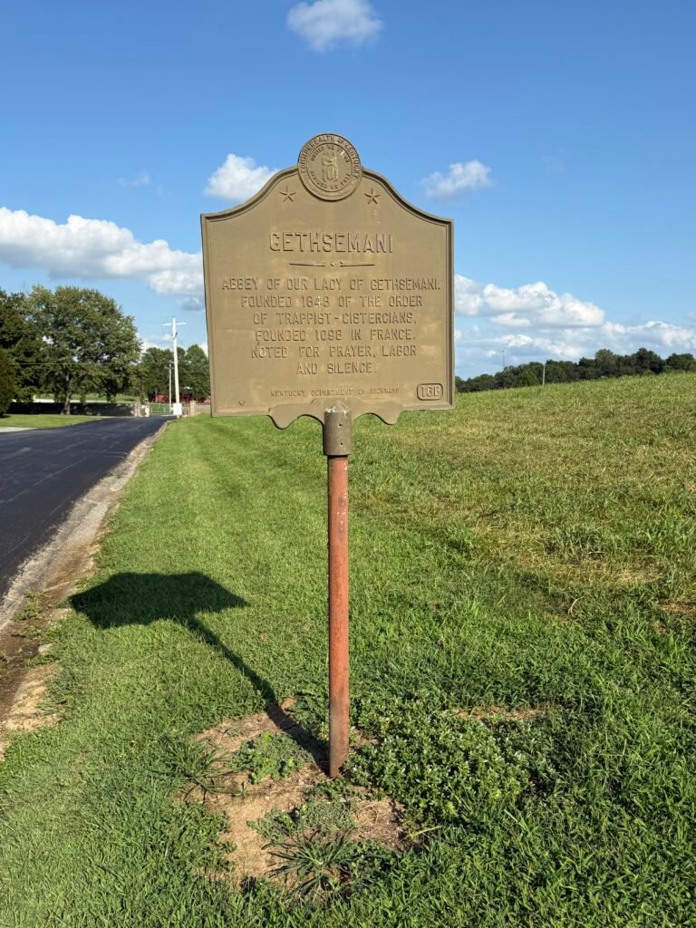 Bronze roadside historical marker for Gethsemani beside a two-lane road