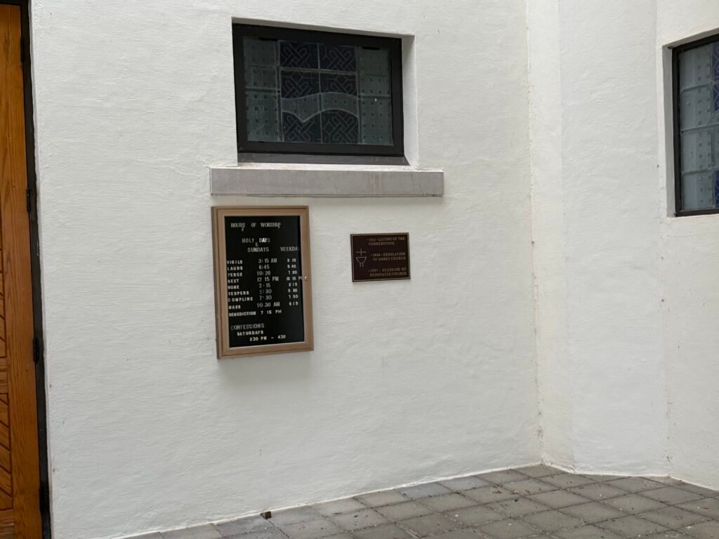 Retreat schedule board mounted on the Abbey's exterior wall, listing daily prayer times