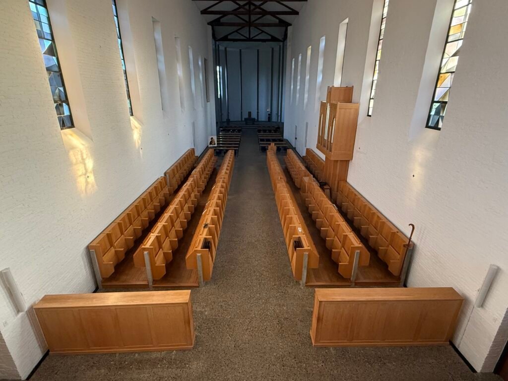 Long church interior hallway with wooden pews, stained glass windows, and exposed timber roof beams