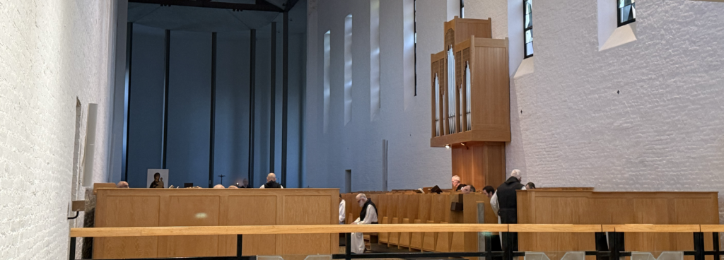Church interior showing choir stalls, organ pipes, and monks seated for prayer