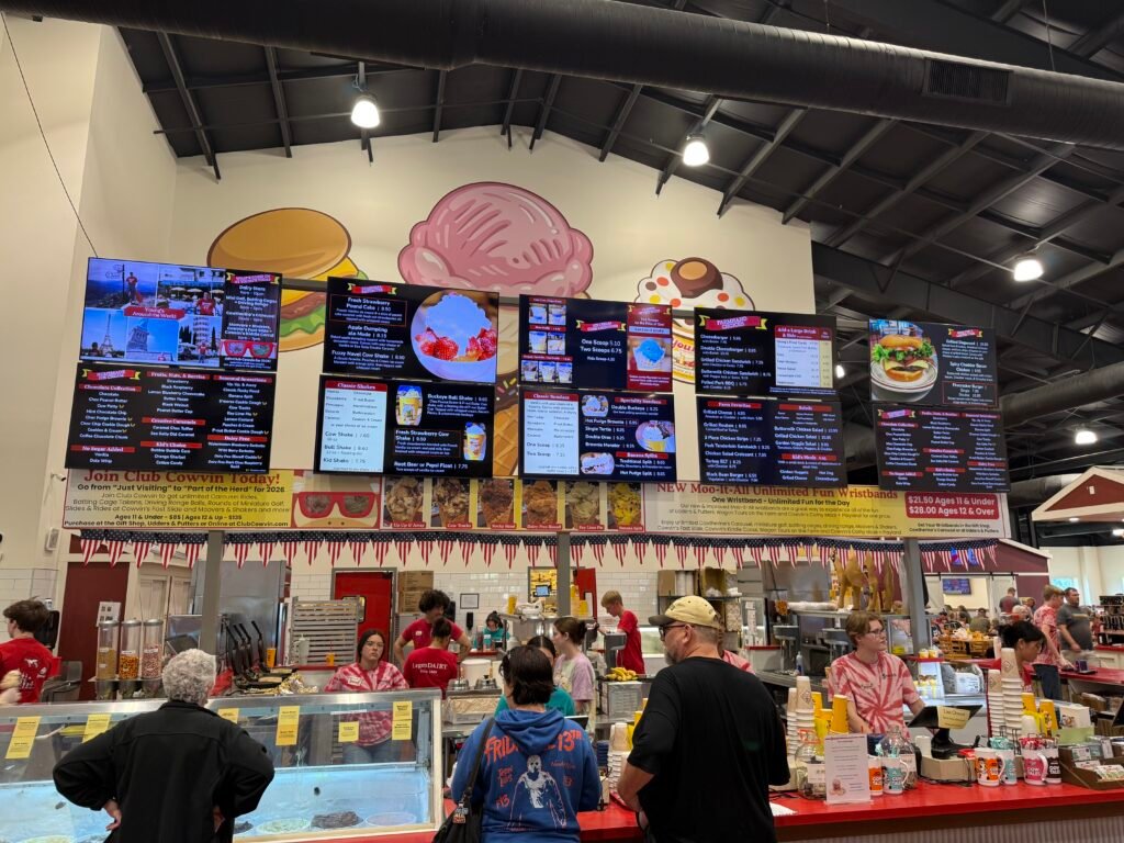 The ordering counter at Young's Jersey Dairy, six lit menu boards mounted overhead and a crowd of customers lined up along a red counter while staff work behind it.