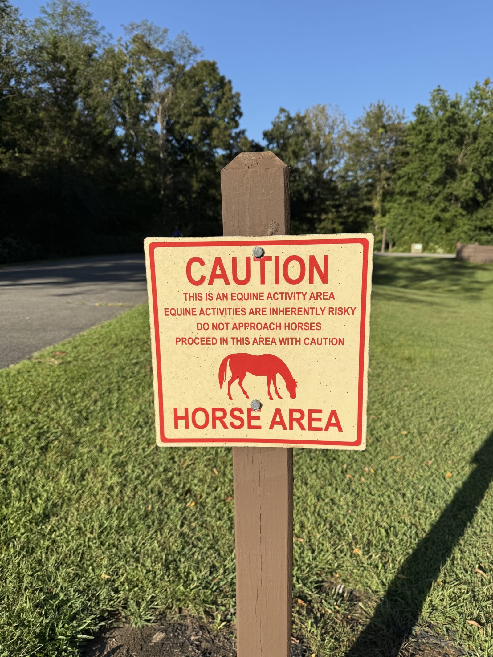 A red and white sign on a wooden post reading Caution, Horse Area, warning that equine activities are inherently risky and that horses should not be approached