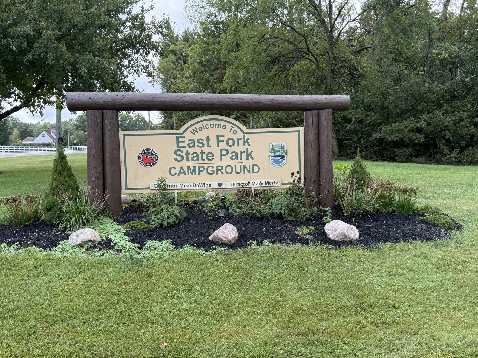 A wooden-framed park sign reading Welcome To East Fork State Park Campground, standing in a landscaped bed of shrubs and stone