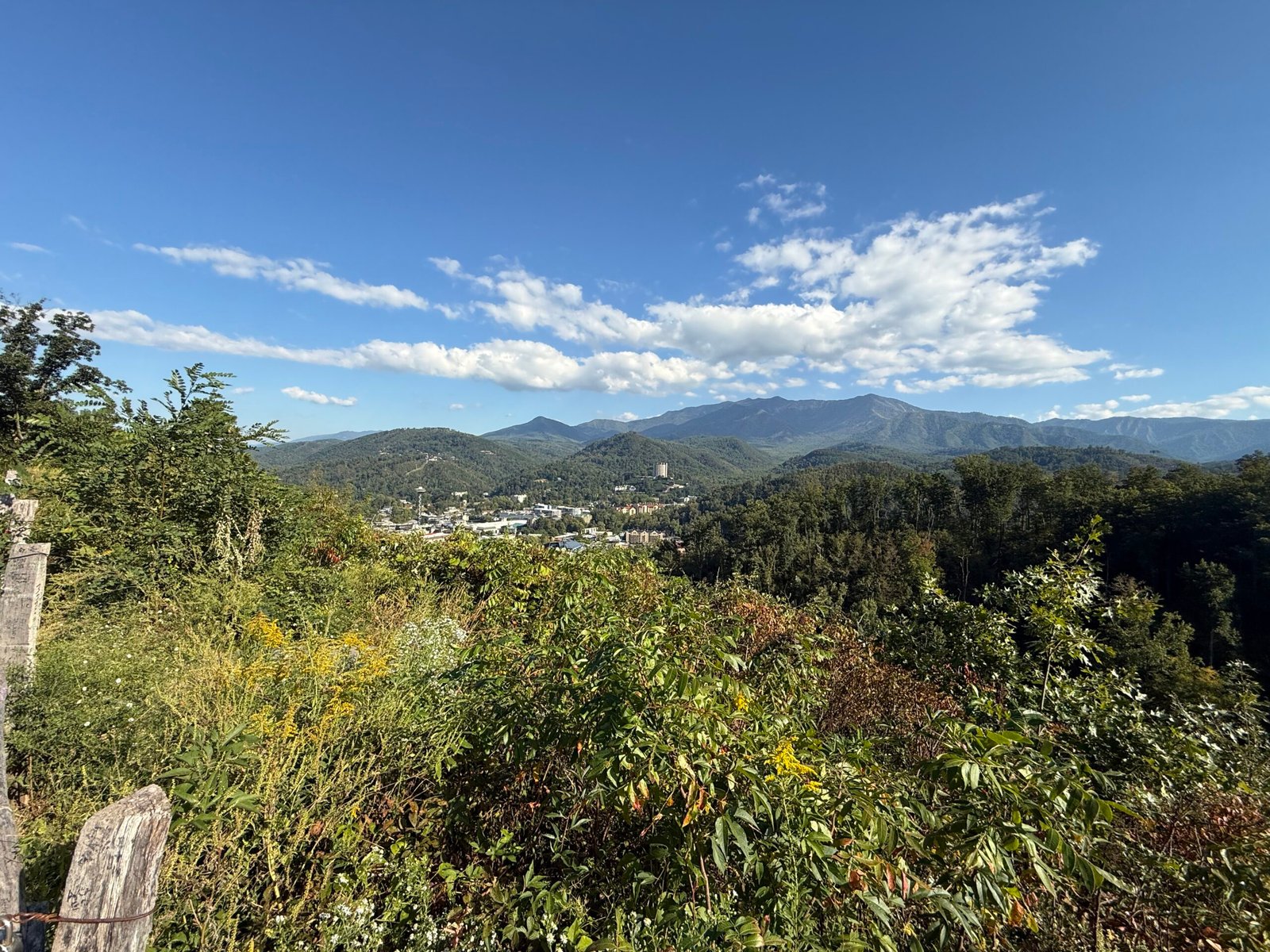 A view over wooded hills and the town of Gatlinburg toward a long mountain ridge under a blue sky
