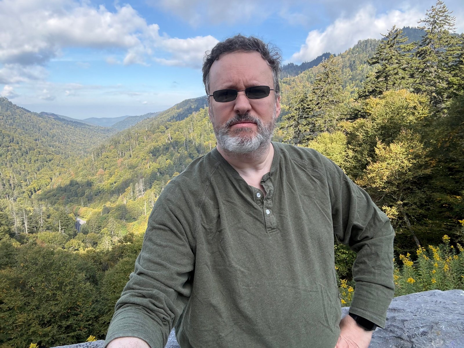 The author in sunglasses and a green henley, with a forested mountain valley behind him