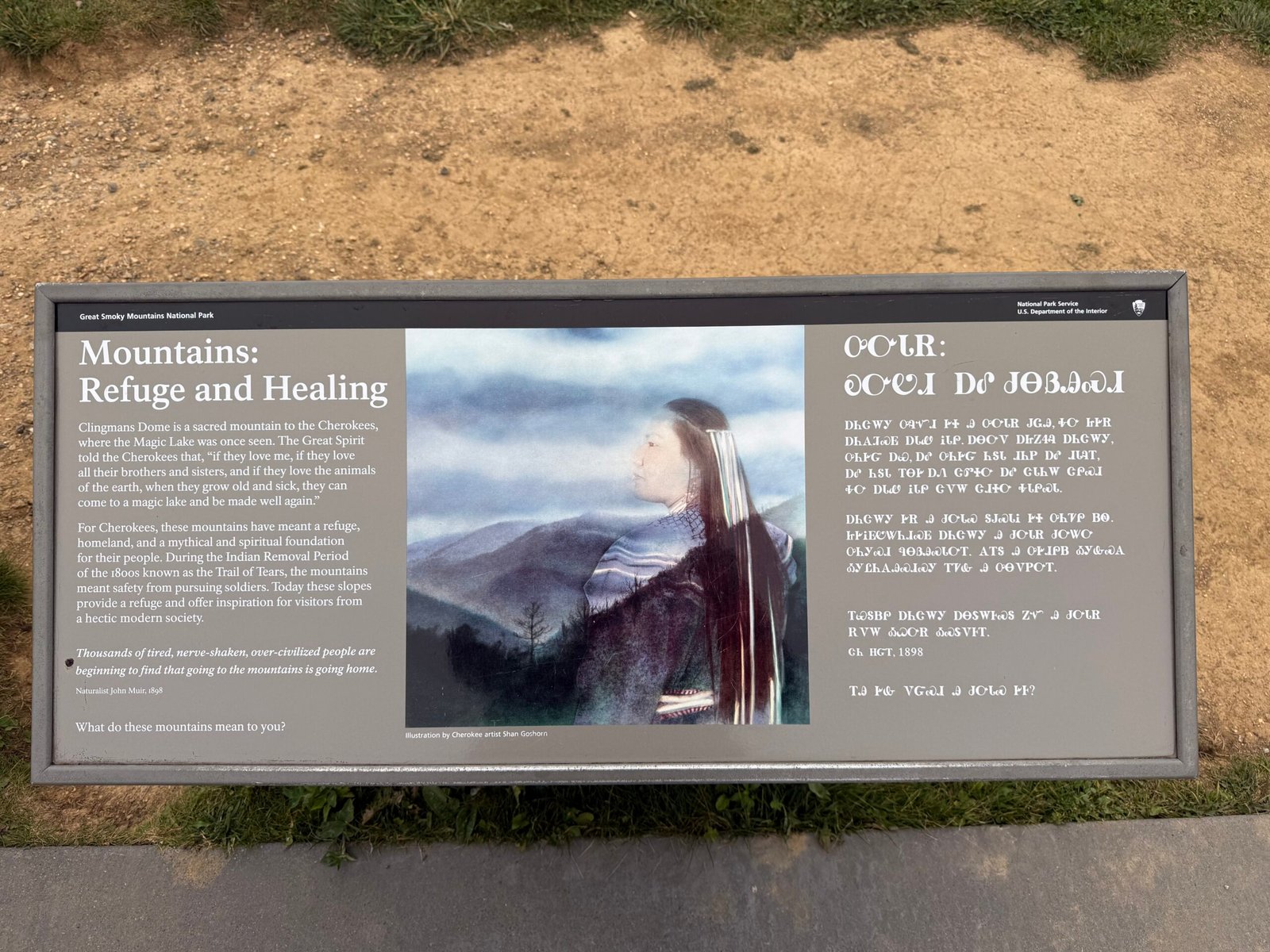 An interpretive panel titled Mountains, Refuge and Healing, with text in English and in the Cherokee syllabary beside a painting of a Cherokee woman before blue mountains