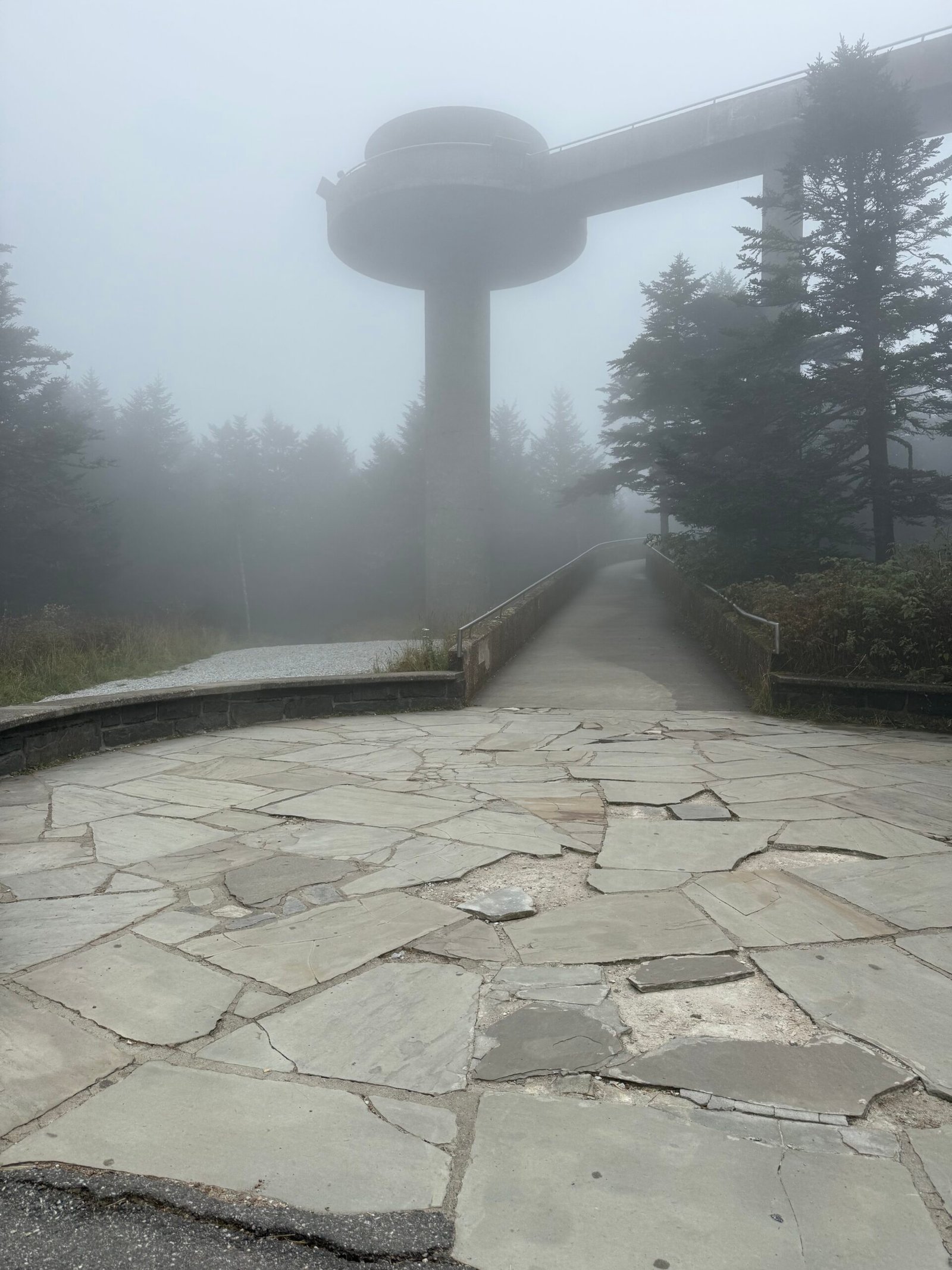 The Kuwohi observation tower and its curving ramp nearly lost in thick fog at the end of a flagstone path