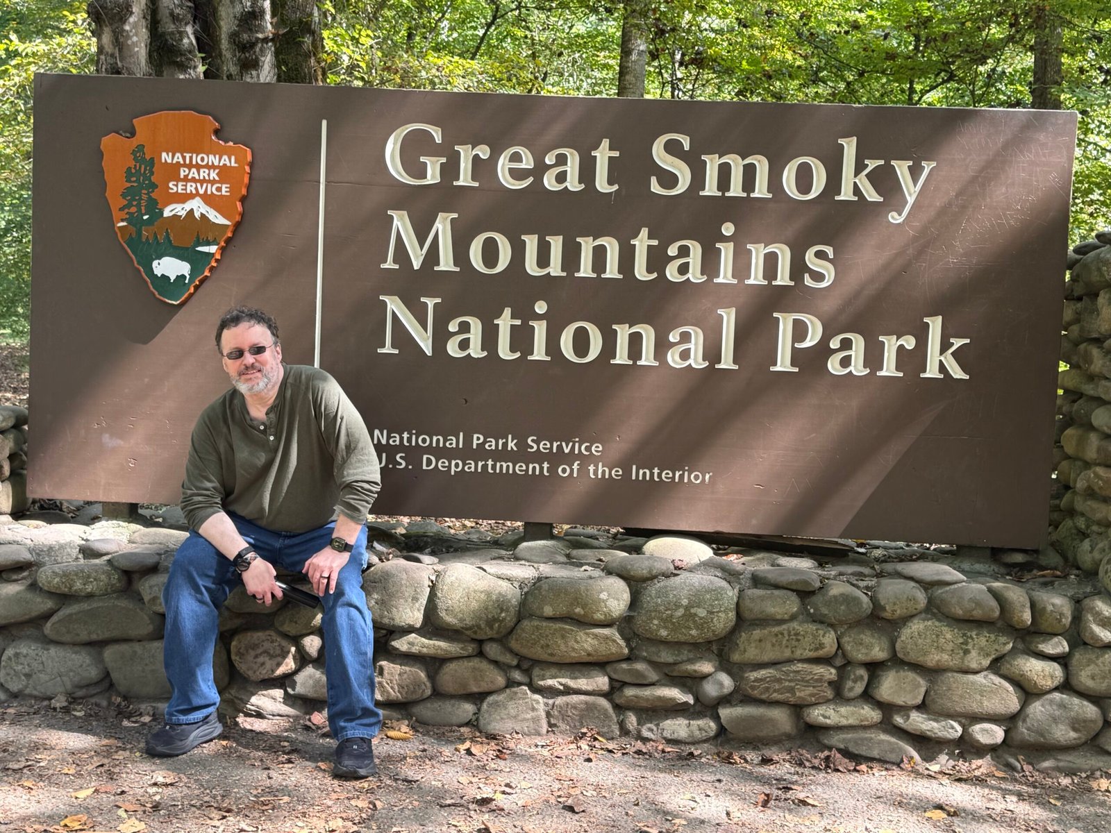 The author sitting on a river-rock wall beneath the brown Great Smoky Mountains National Park entrance sign